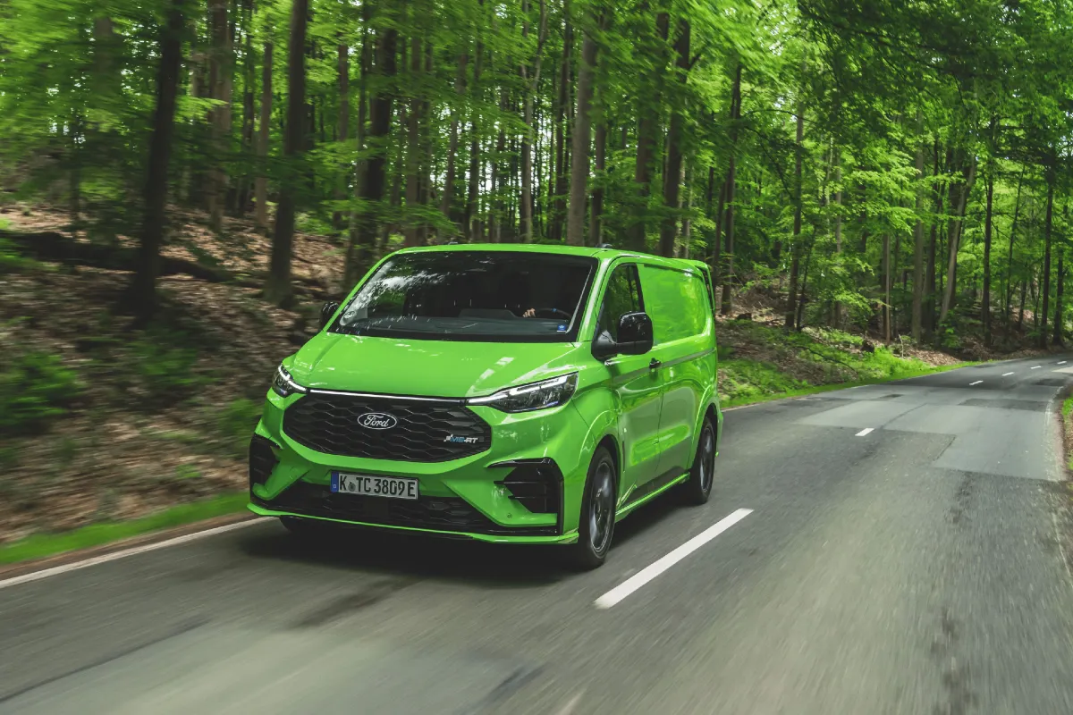 a green ms-rt drives along a road in the woods